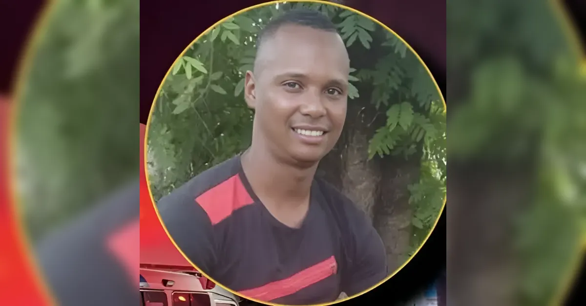 Smiling man in a black shirt with red accents, posed outdoors with green leaves in the background inside a gold circular frame.