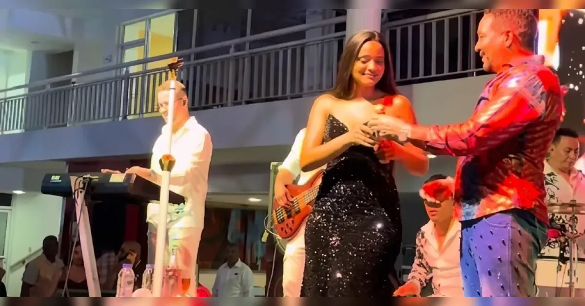 Woman in a black sequined gown on stage accepts a drink from a man in a red shirt while a keyboardist plays nearby.