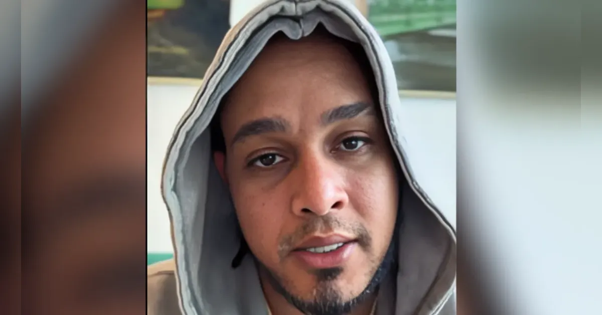 Close-up of a man wearing a gray hoodie, looking into the camera with a neutral expression.