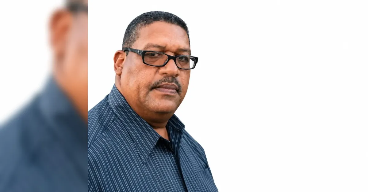 Portrait of a middle-aged man with black-framed glasses wearing a blue striped shirt, against a white background.