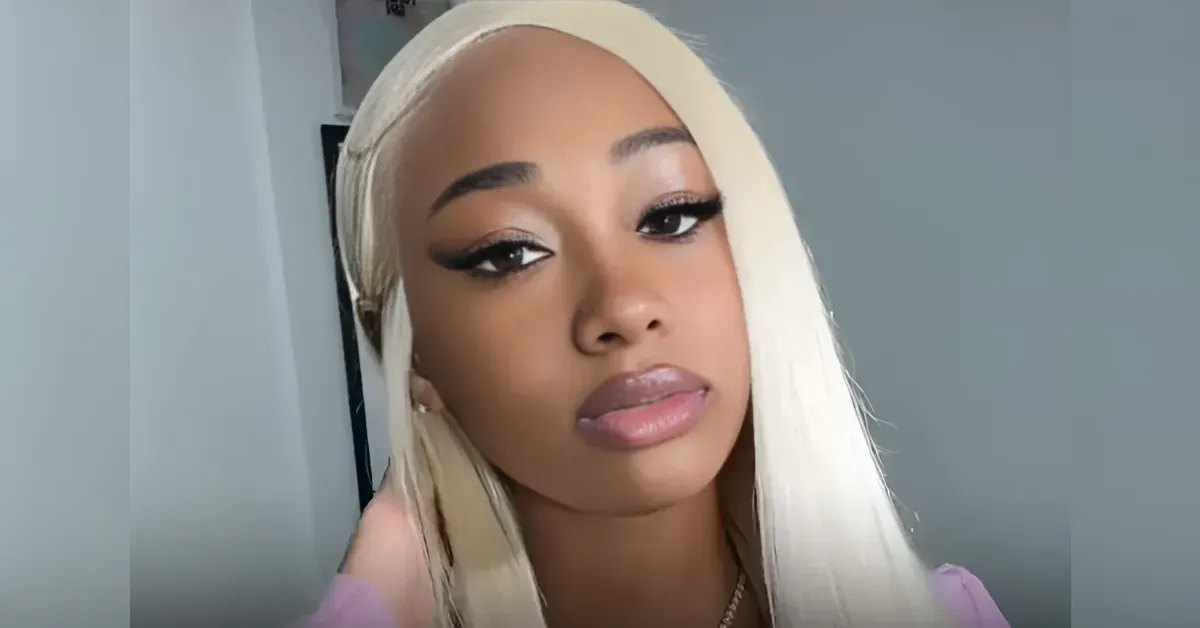 Close-up of a young woman with platinum blonde hair and pink lips, looking at the camera.