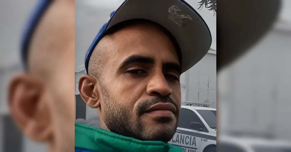Close-up of a man wearing a gray cap, looking at the camera with a police car in the background.