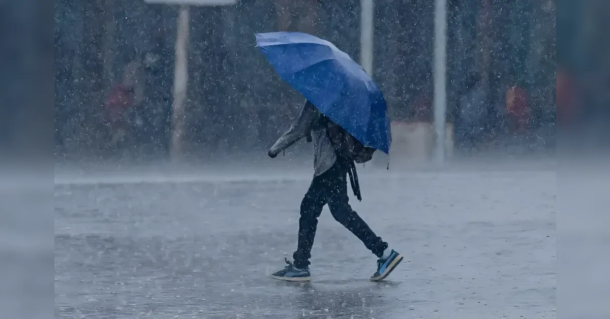 Person walking in heavy rain holding a blue umbrella across a wet street.