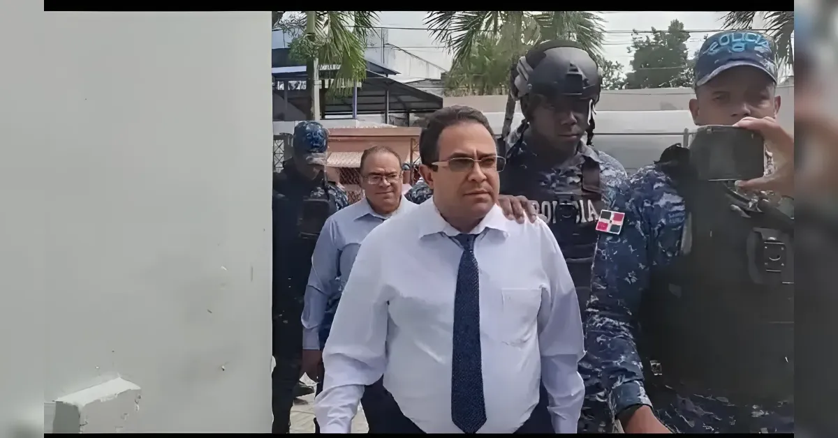 Man in a white shirt and blue tie walks with stern expression while being escorted by uniformed soldiers in tactical gear outdoors.