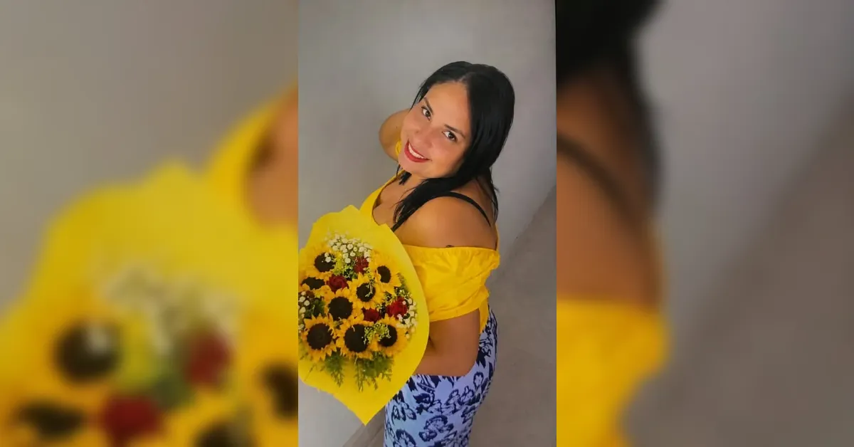 Woman in a yellow off-shoulder top smiling while holding a bouquet of sunflowers toward the camera.
