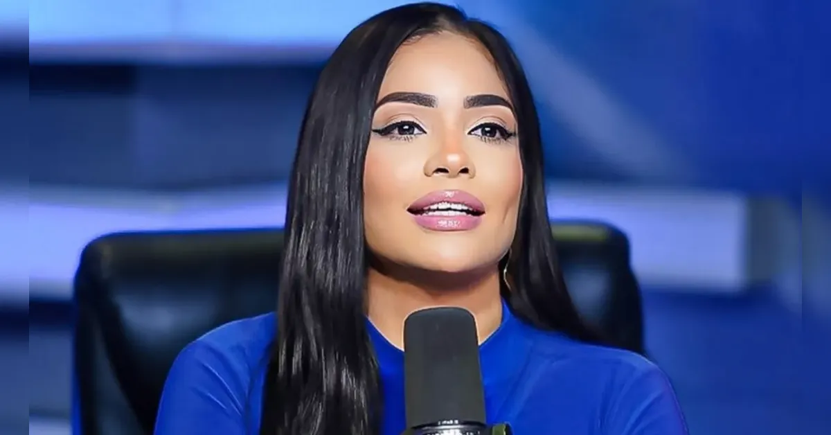 Woman with long black hair in a blue top speaks into a microphone in a studio setting, close-up. (informative)