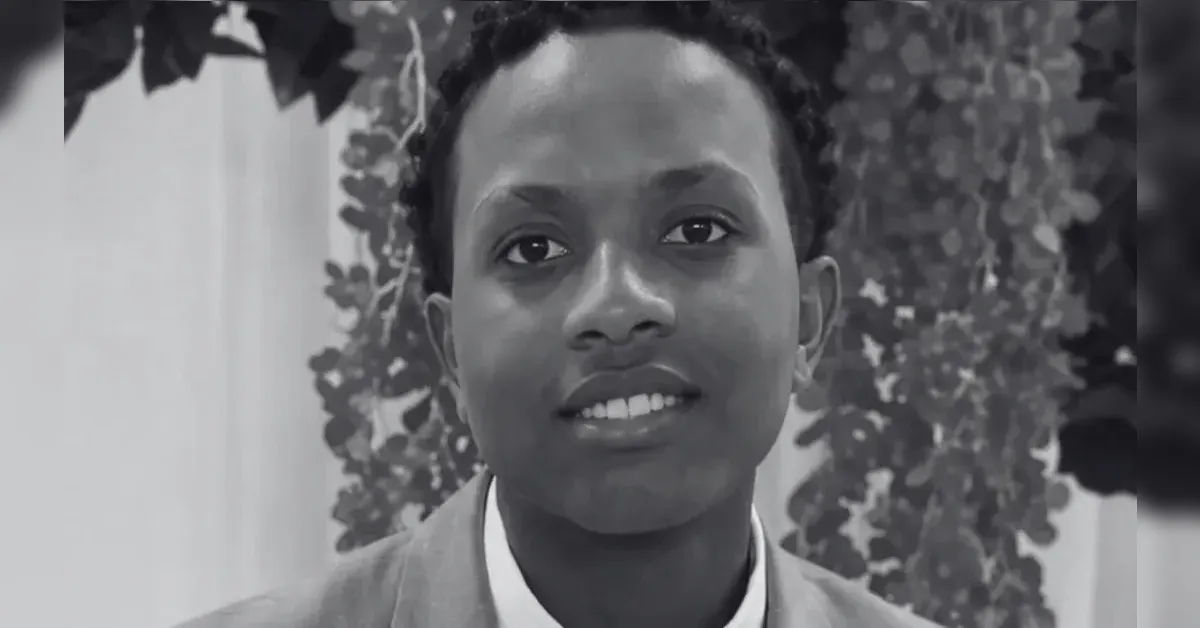 Portrait of a smiling young person in a suit, with leafy background behind them.