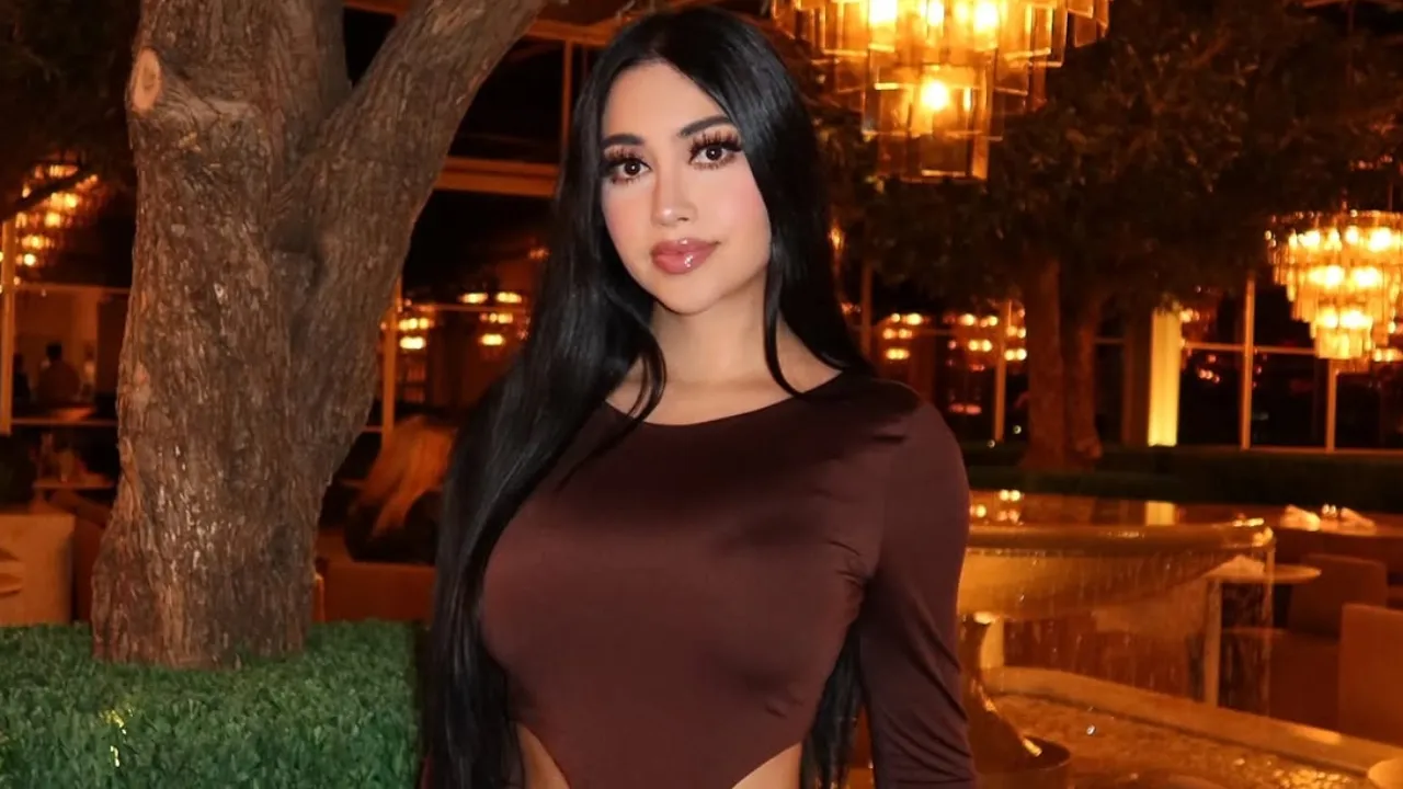 Portrait of a woman with long black hair in a brown long-sleeve top, posing outdoors at night with warm lantern light in the background.