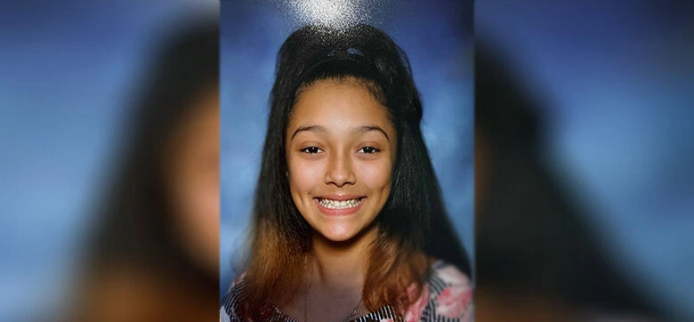 Smiling girl with long dark hair in a school portrait against a blue background.
