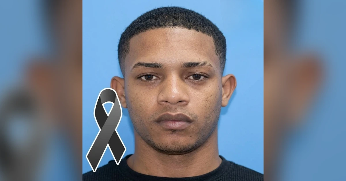 Portrait of a young man against a blue backdrop with a gray awareness ribbon on his left chest area, indicating support or awareness.