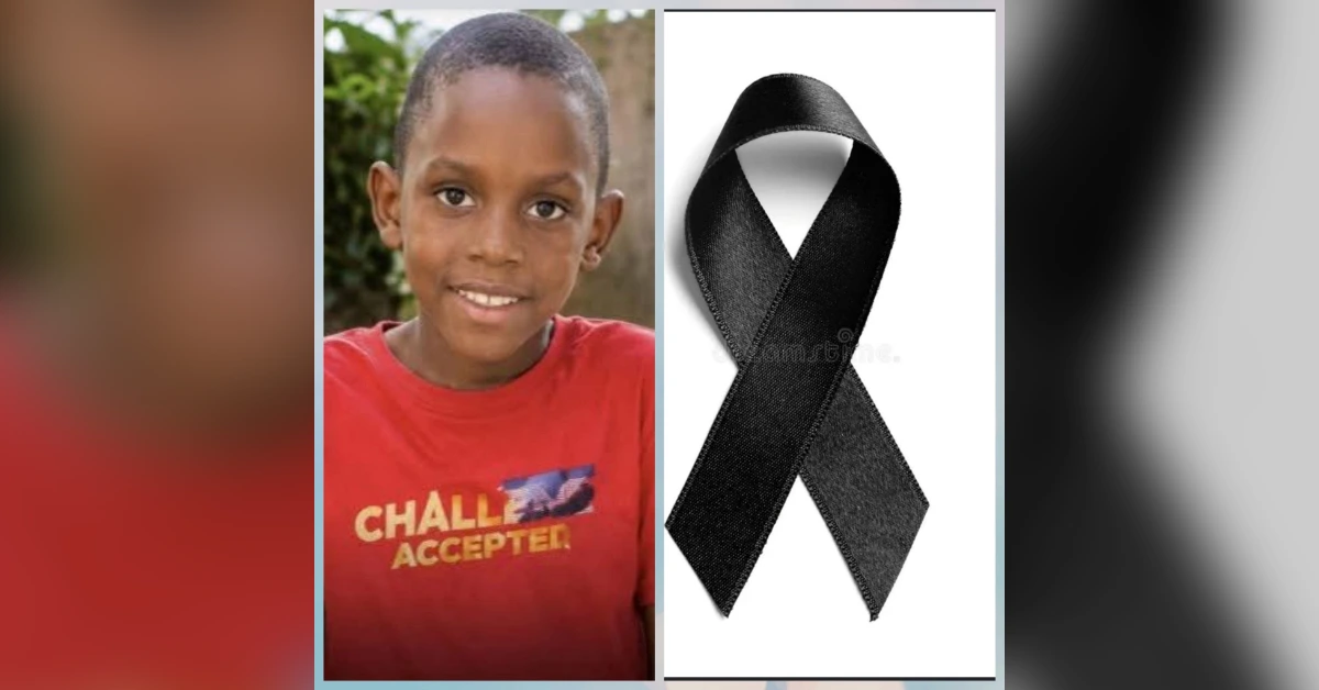 Smiling boy in a red shirt standing outdoors beside a black awareness ribbon.