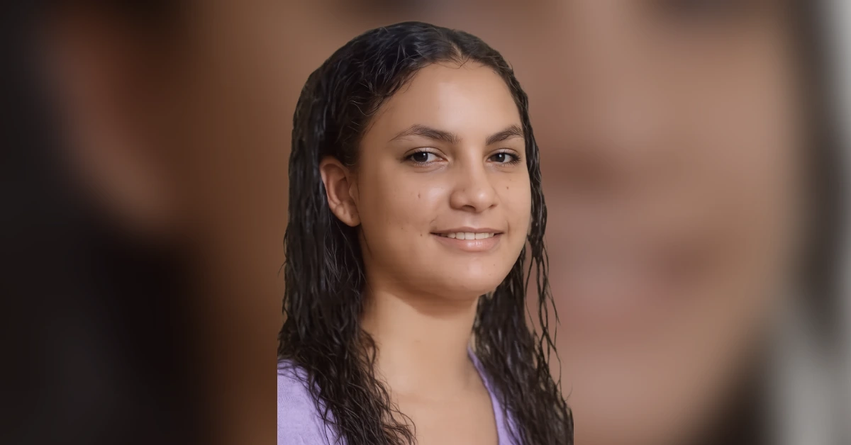 Close-up portrait of a smiling woman with wet hair wearing a lavender top.