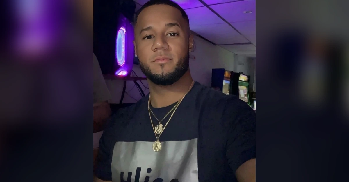 Man selfie in a dim room with purple neon lighting, wearing a black graphic tee and gold chains; arcade machines visible in the background.