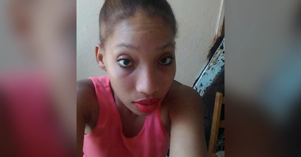 Close-up selfie of a young woman with a high bun, wearing a pink sleeveless top and red lipstick, looking at the camera.