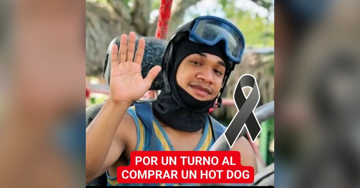 Young man in a helmet and goggles waves at the camera, with a black awareness ribbon and a red banner about taking turns buying a hot dog in Spanish.
