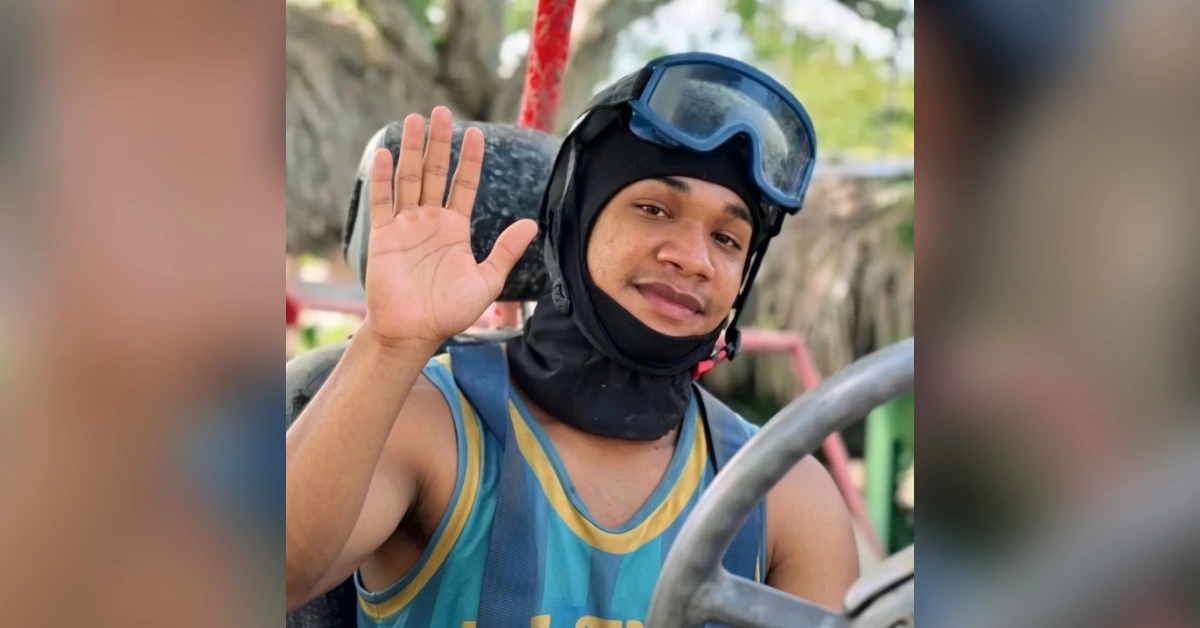 Young man wearing a snorkel mask and helmet, waving from a go-kart or open vehicle.