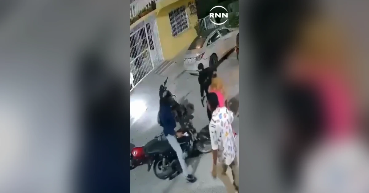 Group of people on a sidewalk confront each other near a parked motorcycle and car; one person points a weapon or object while others watch.