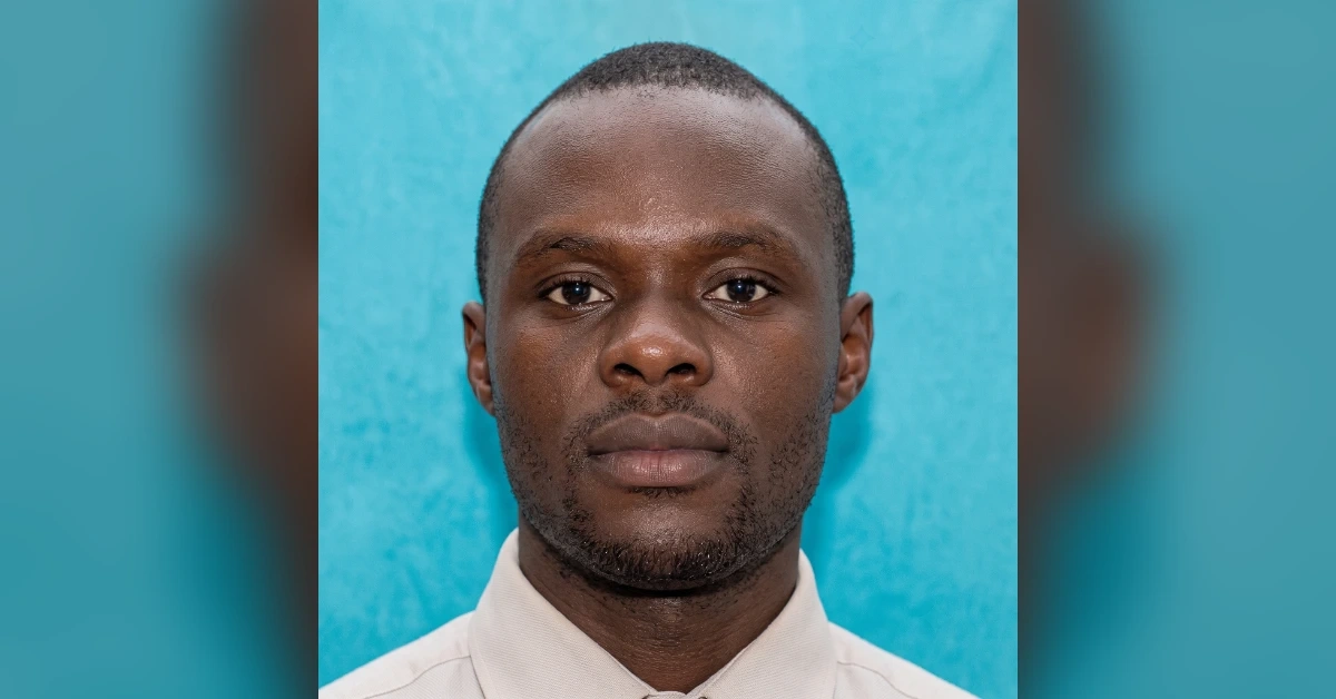 Head-and-shoulders portrait of a man with a neutral expression against a blue background, wearing a light-colored shirt.