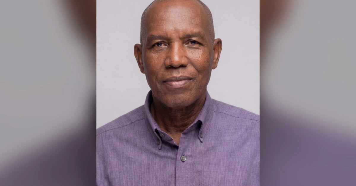 Portrait of an older man with a calm expression wearing a lavender button-down shirt, facing the camera.