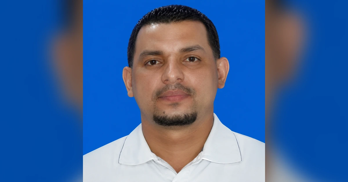 Head-and-shoulders portrait of a man with short dark hair and a goatee, wearing a white polo against a blue background.