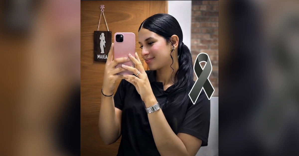 Woman takes a mirror selfie with a pink phone, wearing a black shirt and a gray brain cancer awareness ribbon visible on her chest.