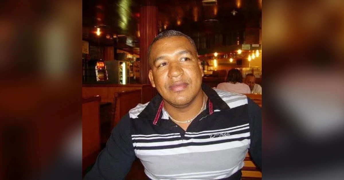 Man sitting at a restaurant table in a black-and-white striped polo shirt, looking to the side in warm lighting.