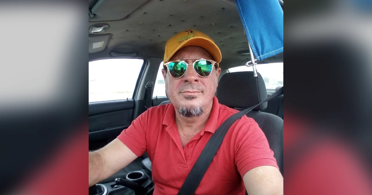 Selfie of a man in a car wearing a red polo, yellow cap, reflective sunglasses, and a seatbelt.
