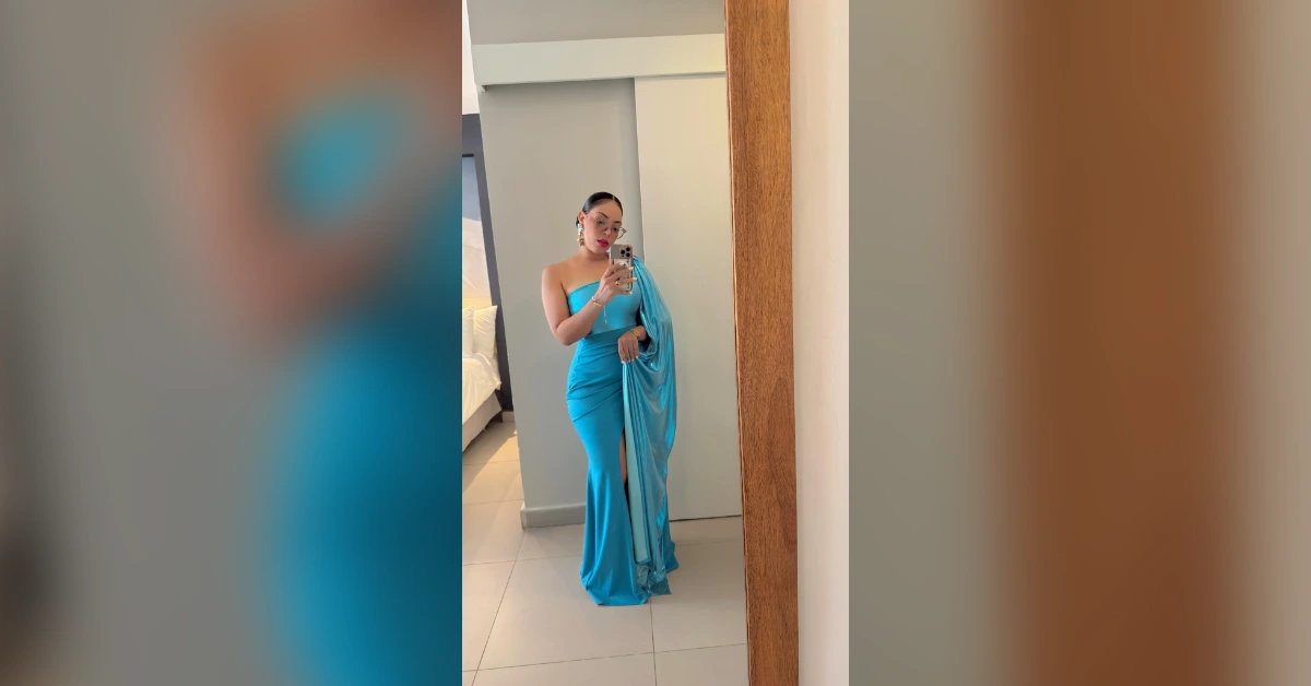 Woman in a turquoise strapless gown with a thigh-high slit, taking a mirror selfie in a bedroom or hotel room.