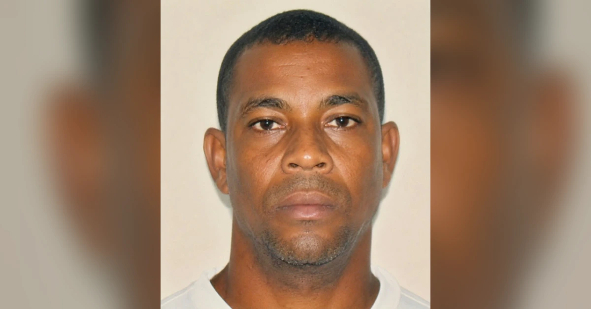 Mugshot-style photo of a man with short black hair, neutral expression, wearing a white shirt against a plain light background