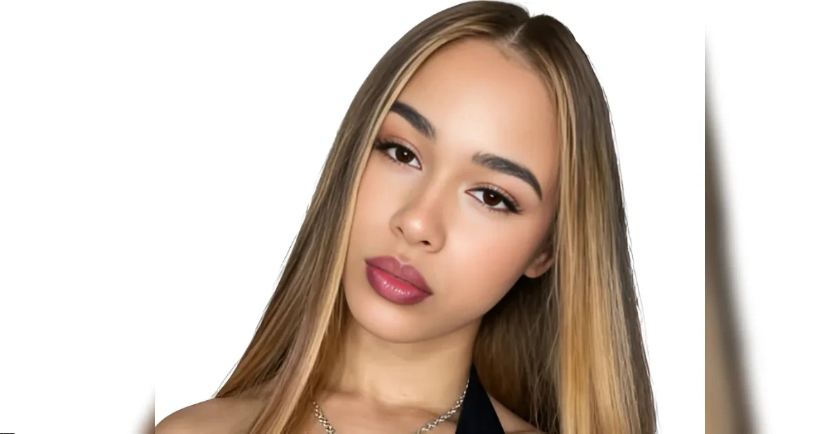 Close-up portrait of a young woman with long, straight hair (dark roots to blonde) and pink lipstick, looking at the camera.