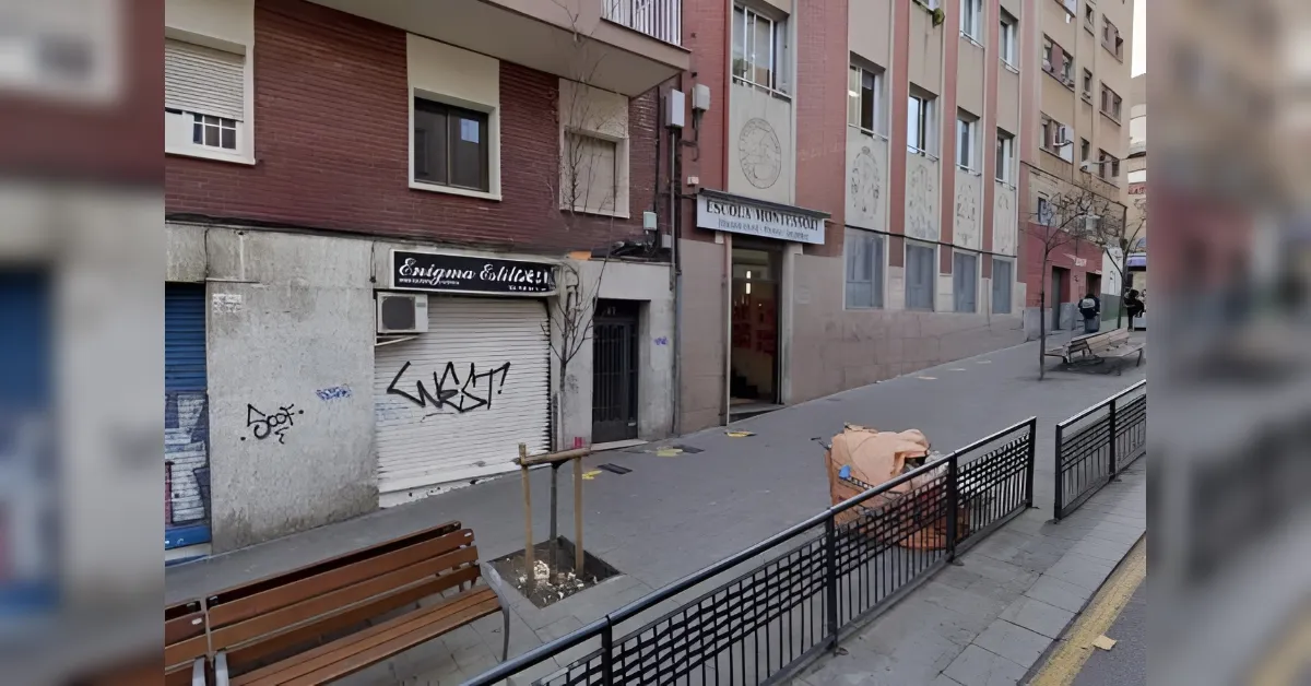 A city sidewalk with a storefront shuttered by a grey metal gate, graffiti on the wall, and a sign above reading a shop name on the left side of the image.