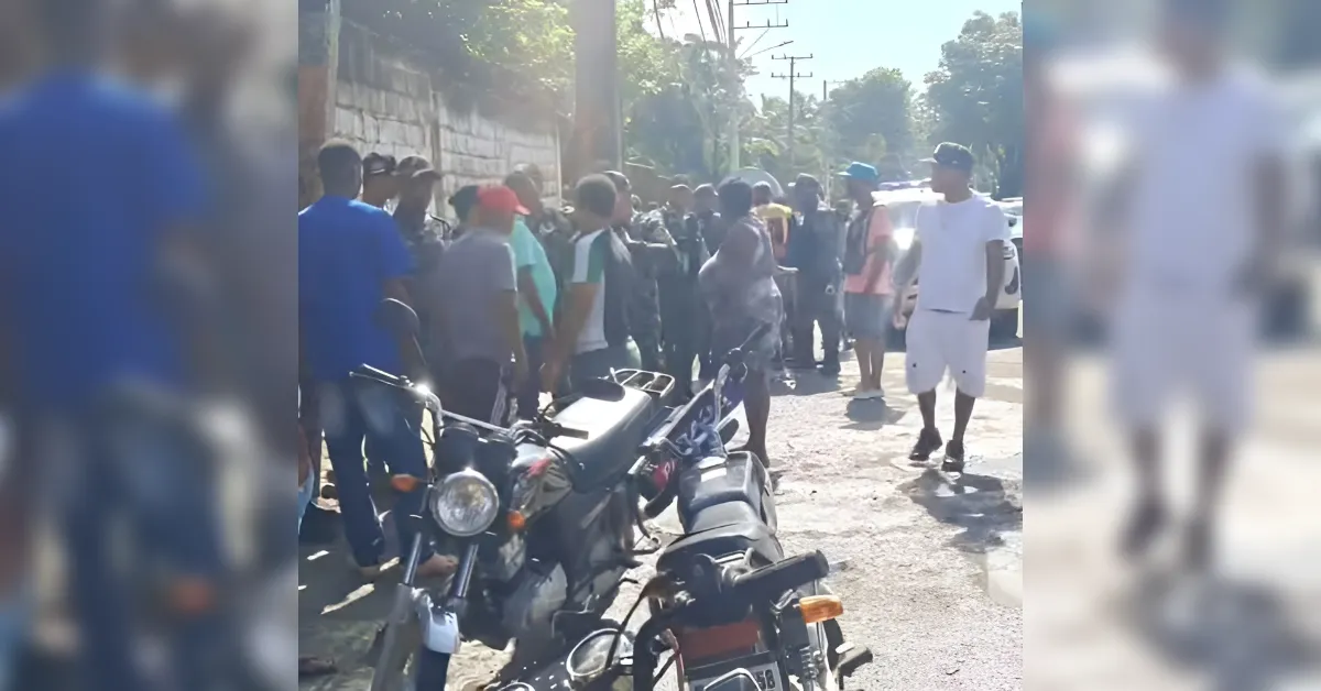 Crowd of people gathered on a sunlit street behind parked motorcycles in the foreground.