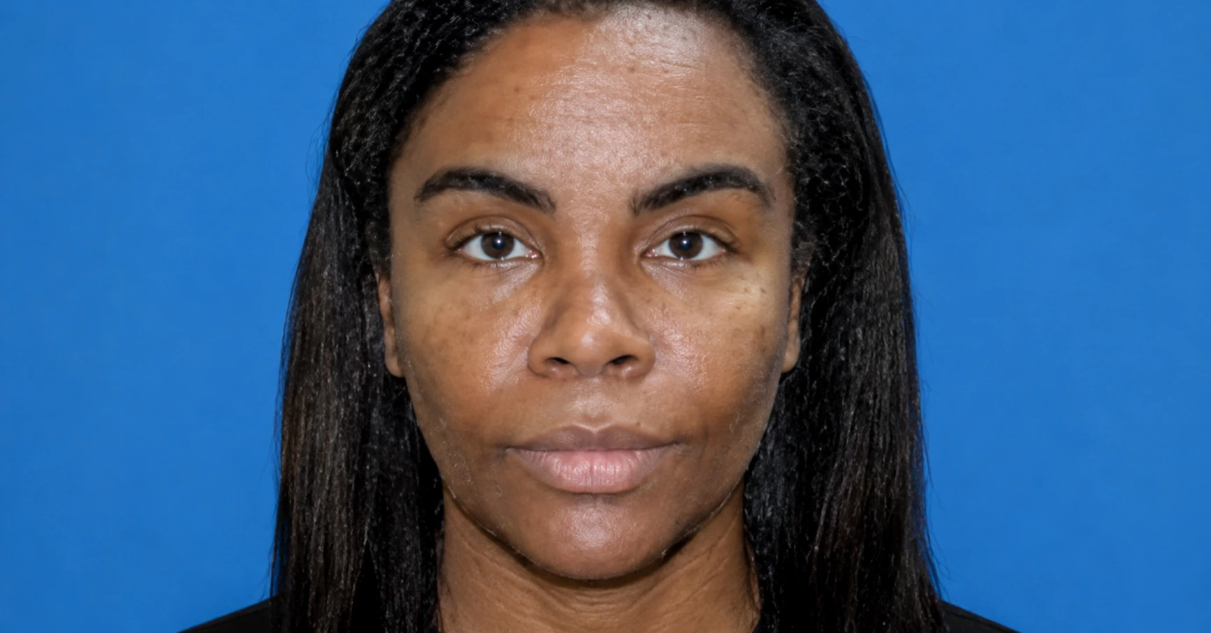 Close-up portrait of a woman facing the camera with a neutral expression against a blue studio backdrop.