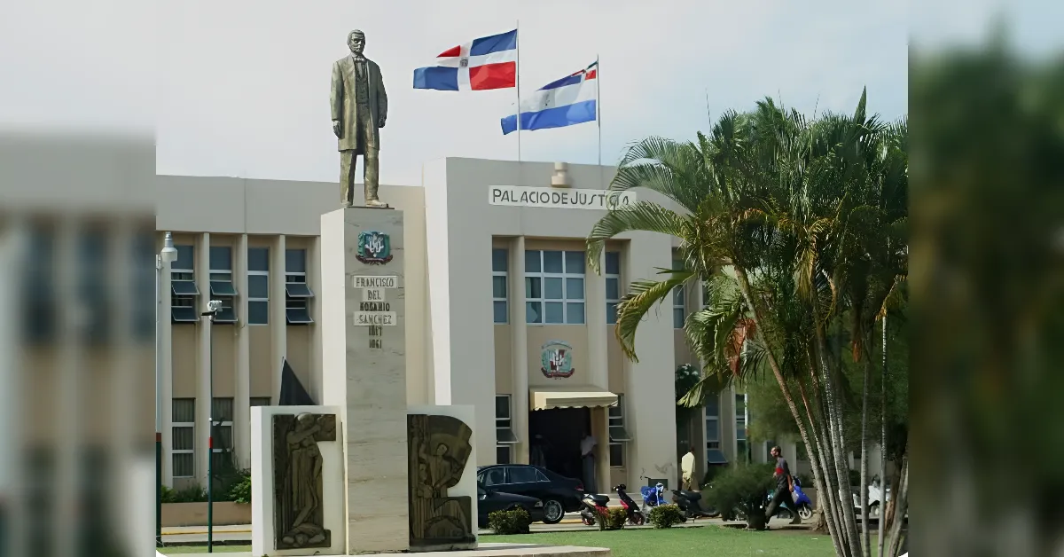 Facade of the Palacio de Justicia courthouse with a tall statue, flags, palm trees, and people near the entrance.