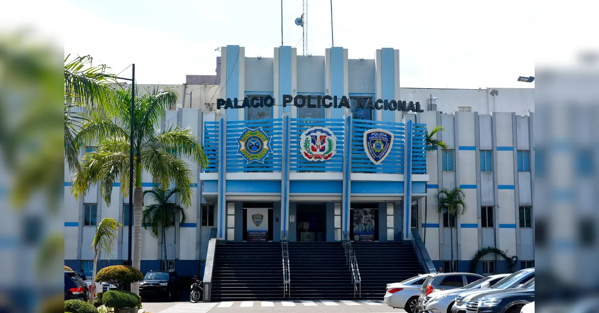 Facade of the Palacio Policia Nacional: a light-blue and white police headquarters with three emblems on the front, wide stairs, and palm trees nearby.