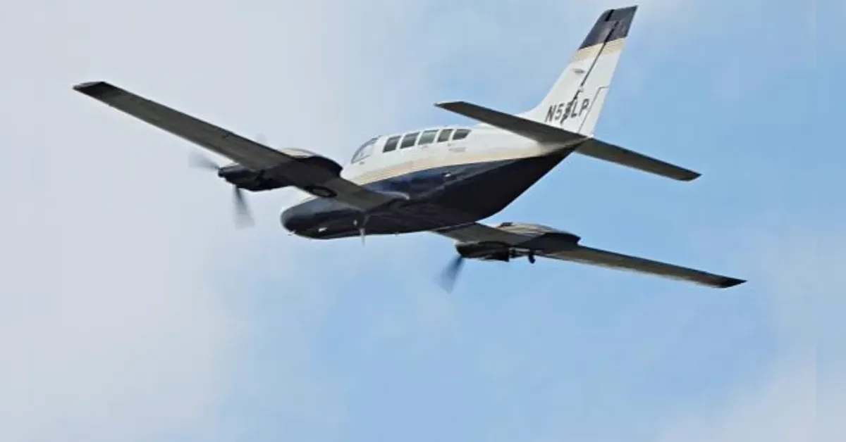Small twin-engine propeller plane in flight against a blue sky, tail number visible on the vertical stabilizer
