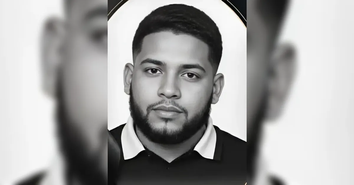 Black-and-white portrait of a young man with short hair and a full beard, wearing a collared polo shirt, looking at the camera.