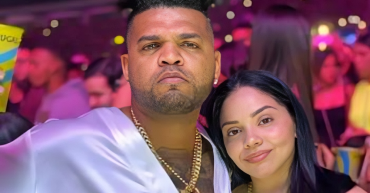 Couple posing for a selfie at a crowded nightclub with pink and purple lighting in the background.