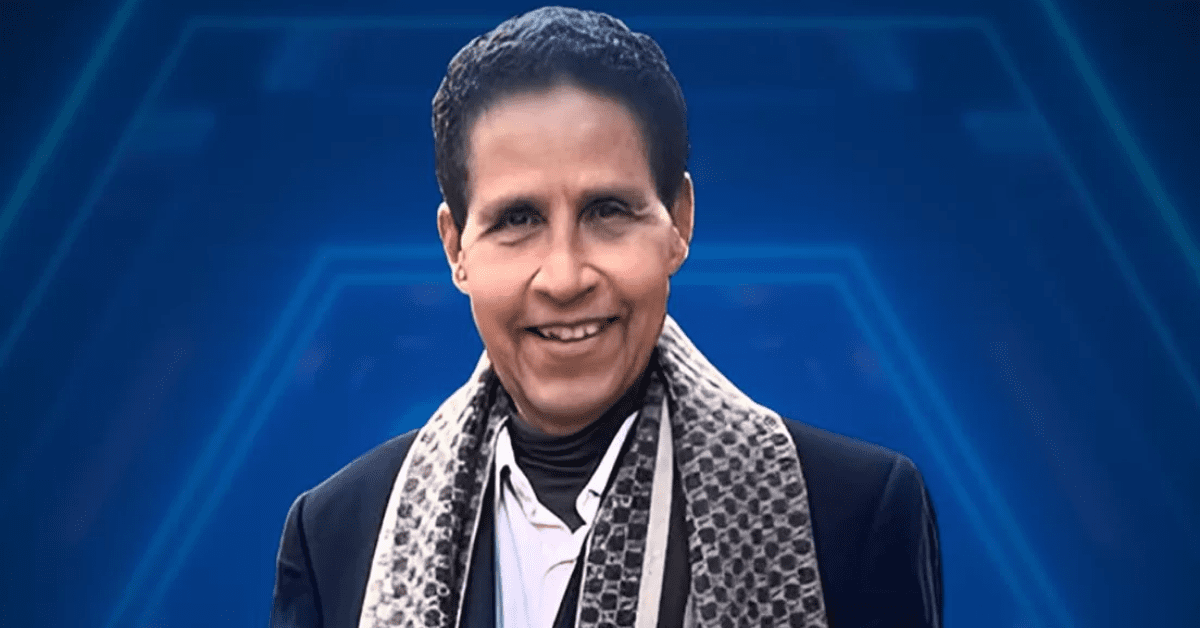 Smiling woman in a black blazer and patterned scarf against a blue geometric background.