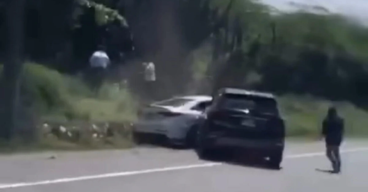 Dark SUV on a highway shoulder with a light-colored car nearby and a person walking along the road behind them, out of focus in the distance.