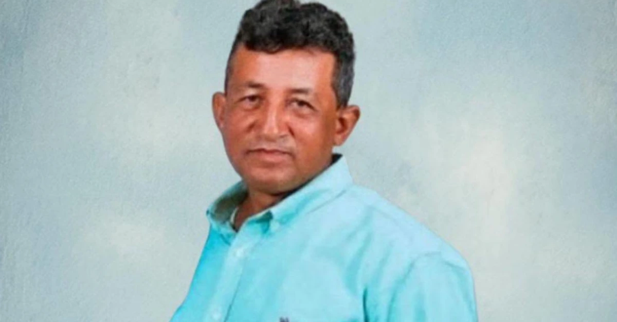 Man in a light blue button-up shirt posing against a pale blue studio backdrop.
