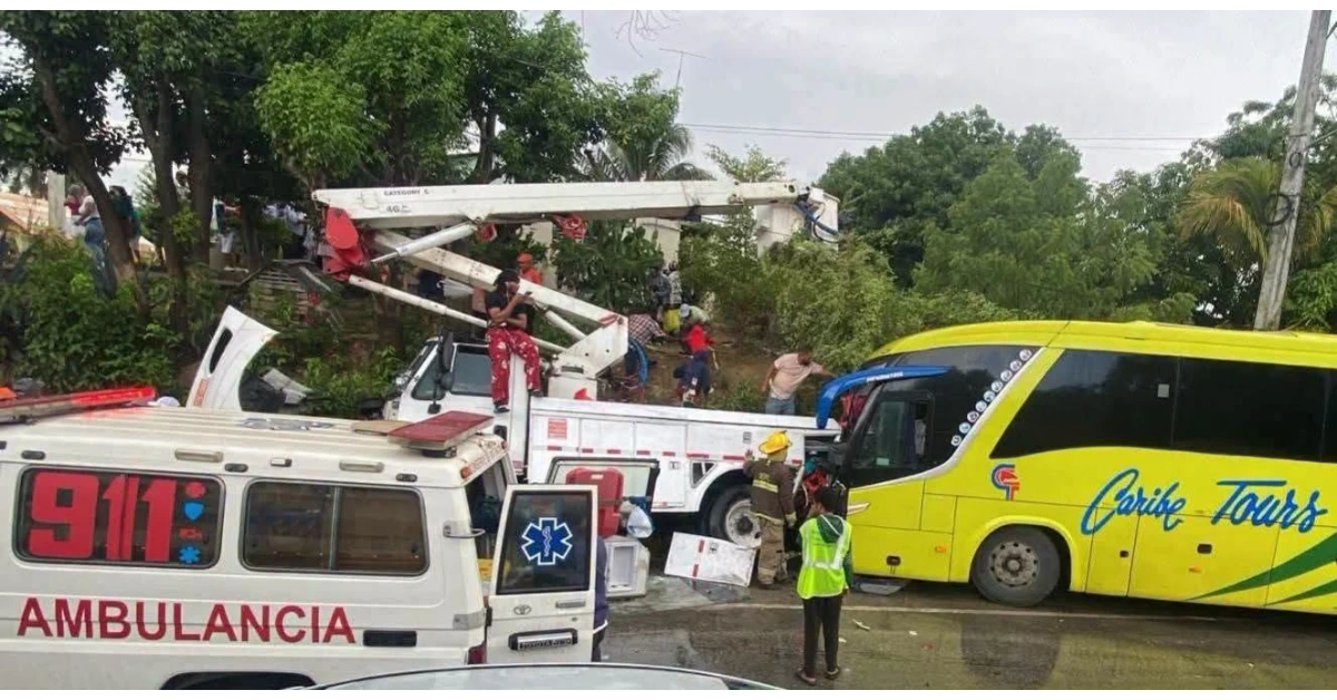 Rescue operation at a bus crash: responders on a crane truck lifting debris while a yellow Caribe Tours bus is nearby in a crowded scene with an ambulance present
