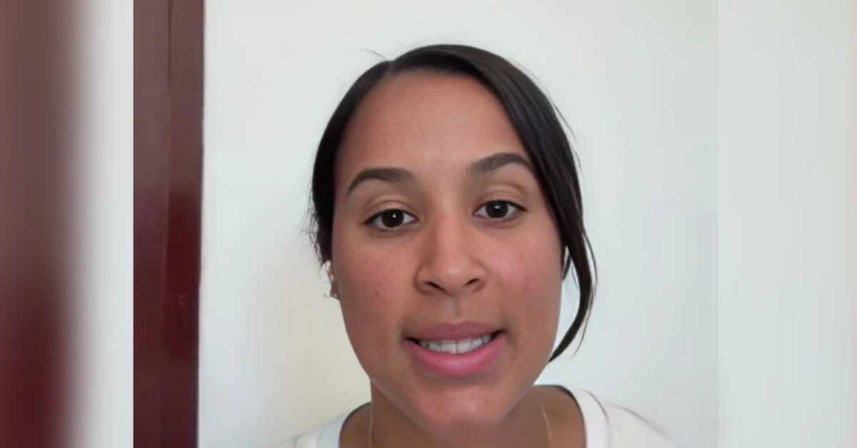 Close-up of a woman speaking directly to the camera in a white shirt with a light wall behind her.