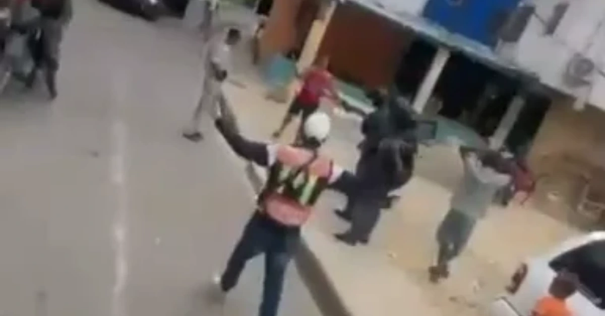 Person wearing a reflective safety vest and white helmet raises arms in a public plaza as bystanders watch.