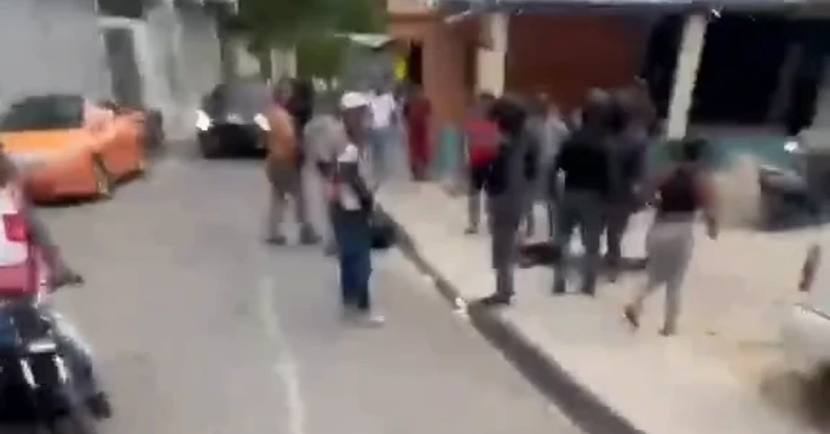 Blurred street scene with a crowd of pedestrians on both sides and a man in the foreground swinging a long object toward the ground.