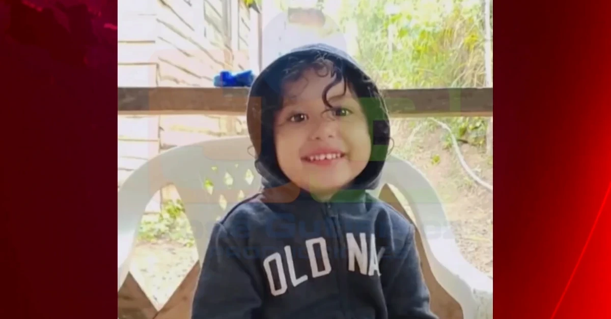 Smiling toddler in a dark hooded sweatshirt sitting on a white plastic chair outdoors.