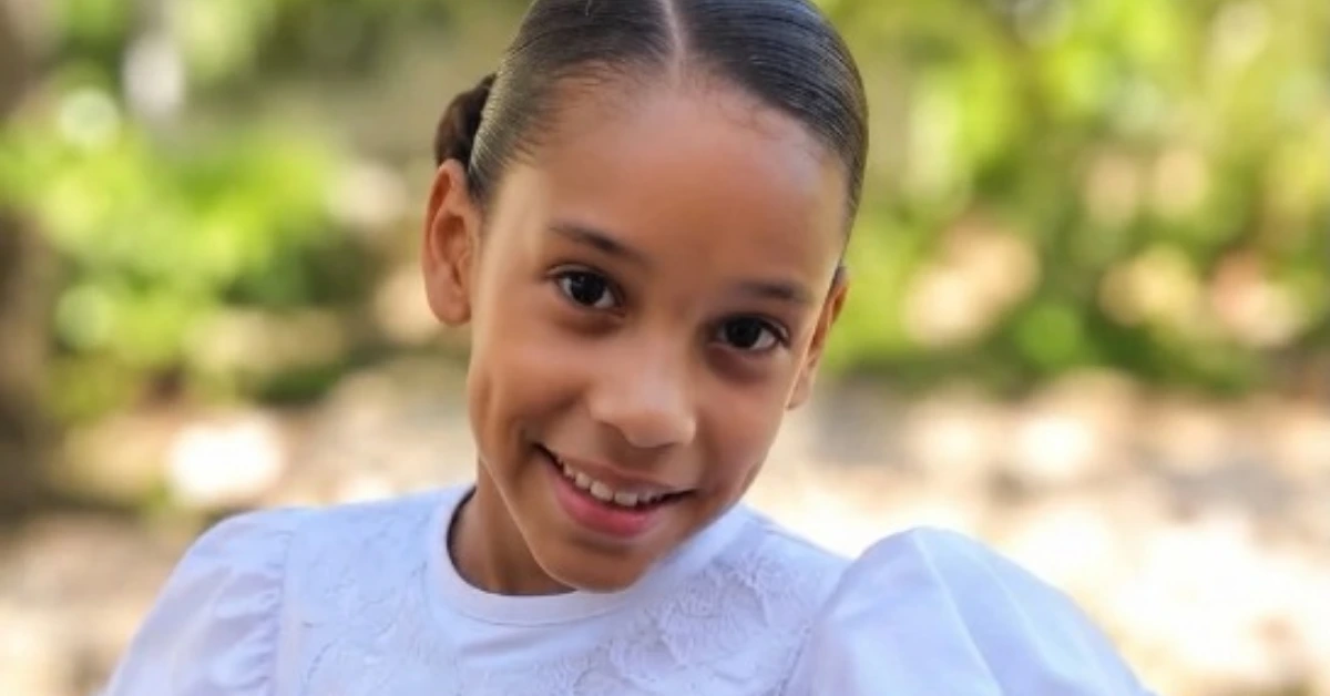 Smiling girl in a white blouse outdoors with a sunlit, blurred green background in the park.