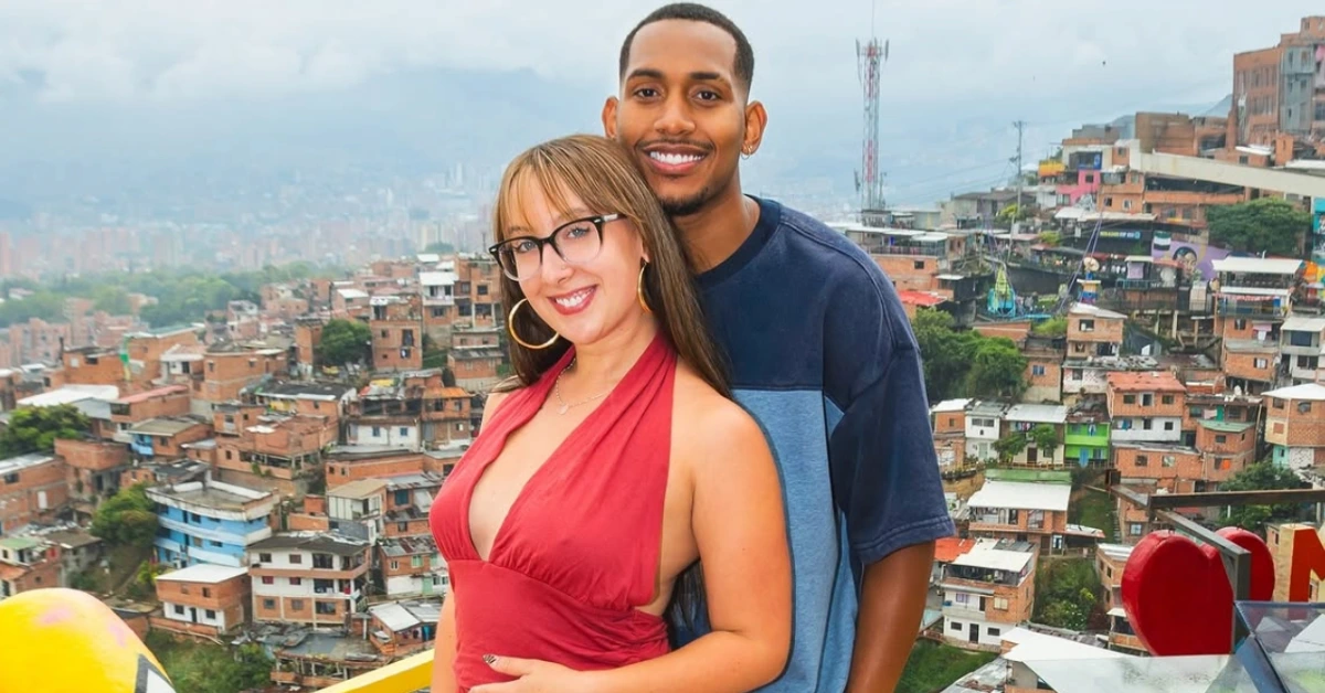A smiling couple posing closely on a balcony with a densely built hillside city behind them.