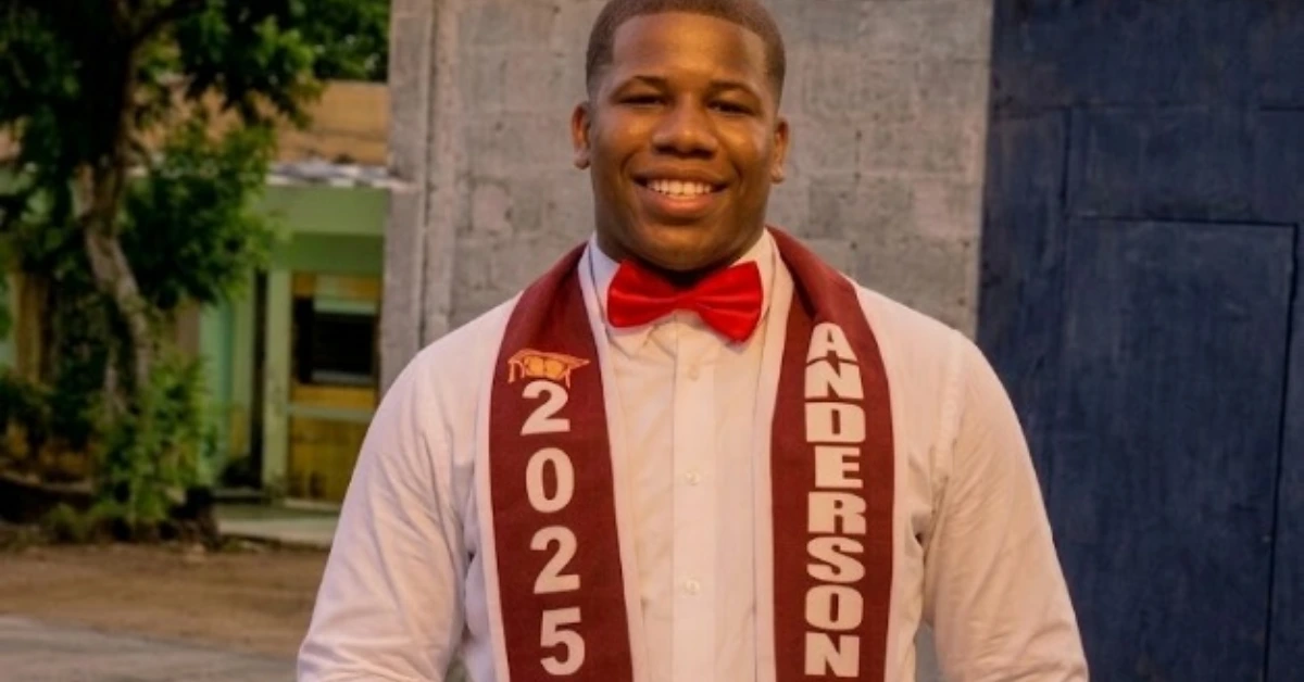 Smiling man in a white shirt and red bow tie wearing a maroon graduation sash that reads 2025 and ANDERSON (outdoors).