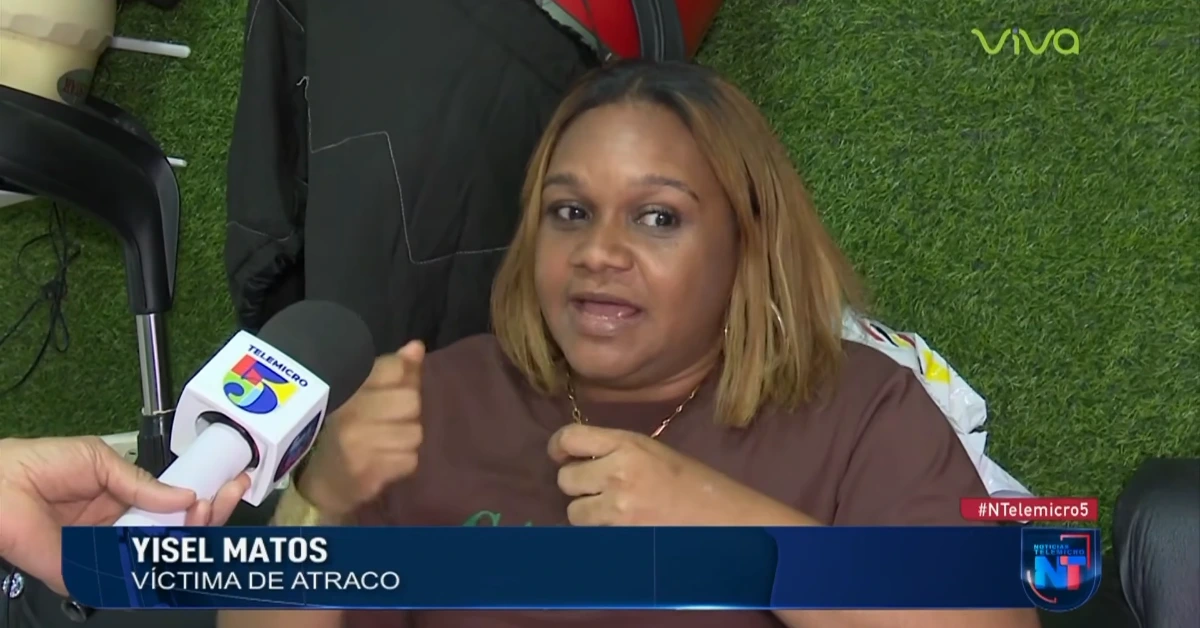 Woman being interviewed on TV, gesturing as she speaks; Telemicro microphone in foreground, chyron reads 'Yisel Matos – víctima de atraco'.